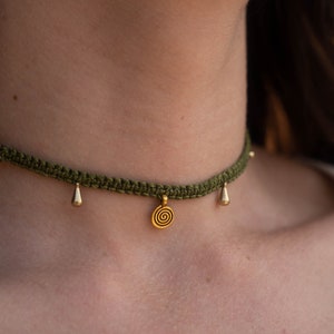 Peut inclure: Un collier ras de cou crocheté vert avec un pendentif en spirale doré et des breloques en forme de goutte d'eau dorées.