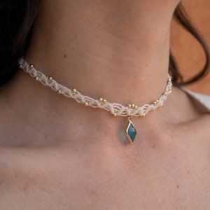 May include: A white macrame choker necklace with gold beads and a blue gemstone pendant.