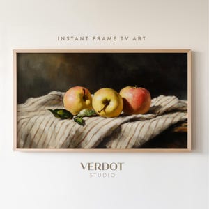 May include: A still life painting of three apples on a striped tablecloth. The apples are red, yellow, and green. The painting is framed in a light wood frame.