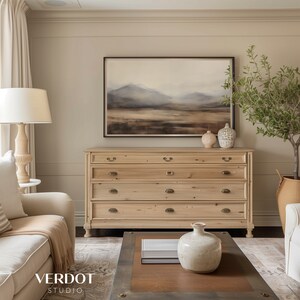 May include: A light wood dresser with five drawers and brass hardware. The dresser is in a living room with a painting of a landscape above it and a vase on top of the dresser.