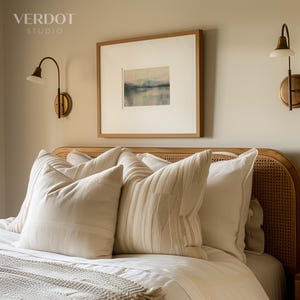 May include: A bedroom with a light brown wicker headboard and a white bed with white pillows and a white blanket. There is a framed abstract painting on the wall above the bed.