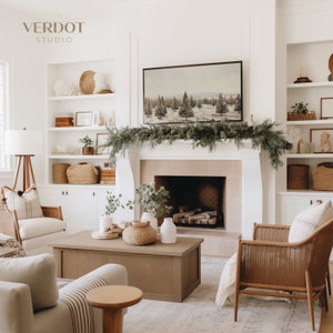 May include: A living room with a white fireplace and a mantel decorated with a green garland. The fireplace has a black grate and a wood-burning fire. There is a brown coffee table in front of the fireplace, and a wicker chair with a white throw blanket on it. There are white shelves on the wall to the right of the fireplace, and a white shelf unit on the wall to the left of the fireplace. The shelves are decorated with various items, including baskets, candles, and plants.
