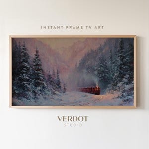 May include: A framed landscape painting of a train traveling through a snowy mountain pass. The artwork features a red train with illuminated windows, surrounded by snow-covered trees and a misty atmosphere. The text "INSTANT FRAME TV ART" and "VERDOT STUDIO" are visible.