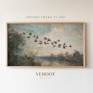 May include: A framed painting depicting a flock of birds in flight over a river and trees. The sky is a pale blue with white clouds. The painting is presented in a light wood frame.