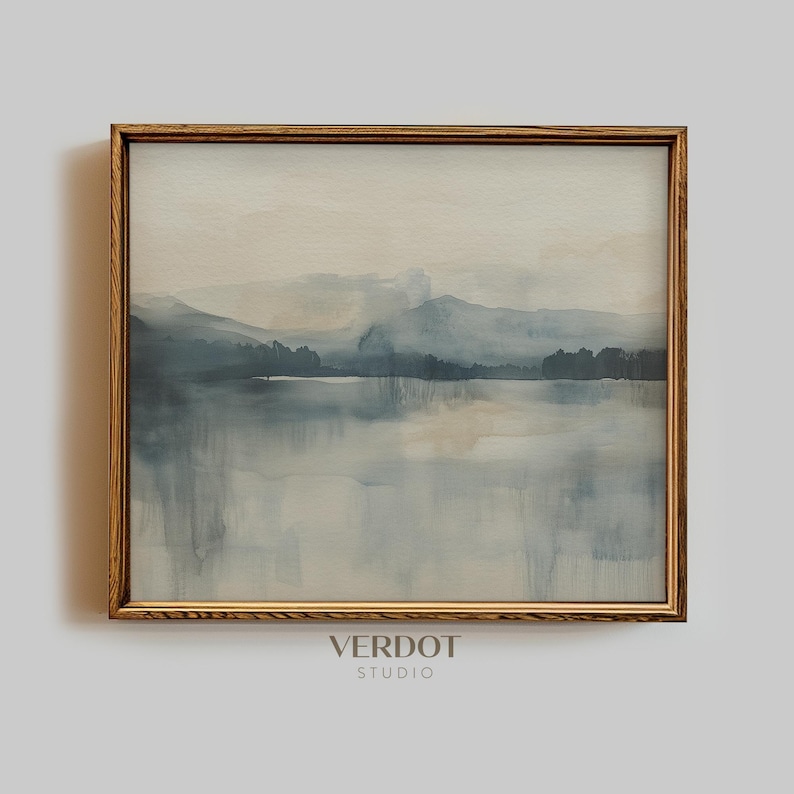 May include: A framed watercolor painting of a misty landscape with a lake in the foreground and mountains in the background. The painting is in shades of blue and gray, with hints of beige and white.