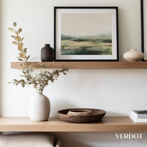 May include: A framed watercolor painting of a landscape with green and brown hues hangs on a wooden shelf. A vase with dried branches and a small ceramic vase are also on the shelf. A wooden bowl and a stack of books are on the lower shelf.