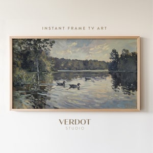 May include: A framed painting of a lake scene with trees and ducks. The painting is in a light wood frame and has a light blue background with a cloudy sky. The lake is calm and reflective, and the ducks are swimming in the water. The text "INSTANT FRAME TV ART" is at the top of the image, and the text "VERDOT STUDIO" is at the bottom of the image.