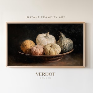 Peut inclure: Impression numérique encadrée représentant une nature morte de citrouilles dans un style sombre et mélancolique. Les citrouilles, blanches et orangées, sont disposées dans un bol marron. Le texte "INSTANT FRAME TV ART" est en haut.