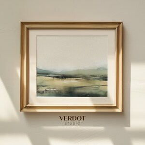 May include: A framed abstract watercolor painting in shades of green and gold. The painting depicts a landscape with hills and water. The frame is a light wood color. The text "VERDOT STUDIO" is printed below the frame.
