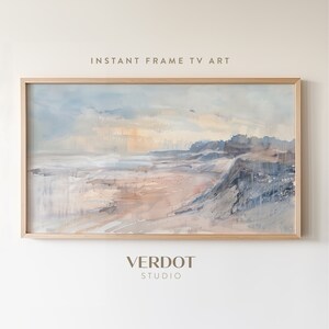 May include: A framed watercolour painting of a seascape with a sandy beach, blue water, and a cloudy sky. The painting is in a light wood frame.