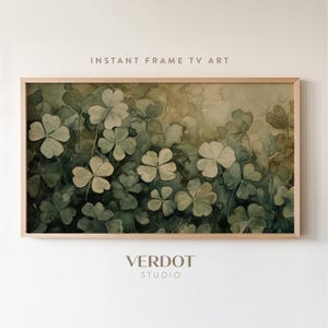 May include: A watercolor painting of green four-leaf clovers on a brown background. The painting is framed in a light wood frame.