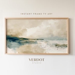 May include: A framed watercolor painting of a seascape with a sandy beach, blue water, and a green hill in the background. The painting has a light brown and beige color scheme. The frame is a light wood color. The text "INSTANT FRAME TV ART" is at the top of the image and the text "VERDOT STUDIO" is at the bottom of the image.
