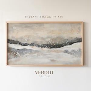 May include: Abstract landscape painting in shades of beige, grey, and black. The painting depicts a series of rolling hills with a white, cloudy sky above. The painting is framed in a light wood frame. "INSTANT FRAME TV ART" and "VERDOT STUDIO" are printed below the painting.