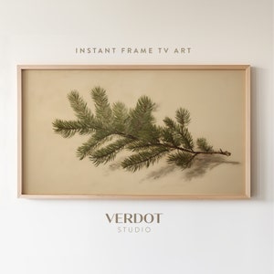 May include: A framed print of a green pine branch with a light brown background. The frame is a light wood color. The text "INSTANT FRAME TV ART" is above the image and "VERDOT STUDIO" is below the image.