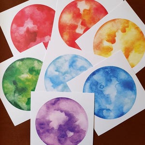 Könnte beinhalten: Eine Sammlung von Aquarelldrucken mit farbenfrohen Himmelskugeln. Die Drucke zeigen eine Vielzahl von Farbtönen, darunter Rot, Orange, Gelb, Grün, Blau und Lila. Jeder Druck hat eine einzigartige Aquarelltextur und ist vor weißem Hintergrund angeordnet.