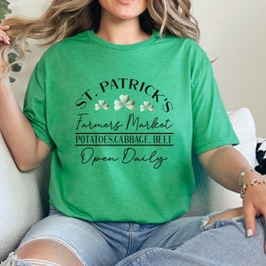 May include: Green t-shirt with a black graphic that says "St. Patrick's Farmers Market Potatoes, Cabbage, Beef Open Daily" with shamrock designs.