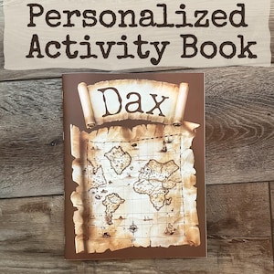 May include: A personalized activity book with the name "Dax" on the cover. The cover features a vintage map design with a scroll banner. The book is brown with a wooden background.