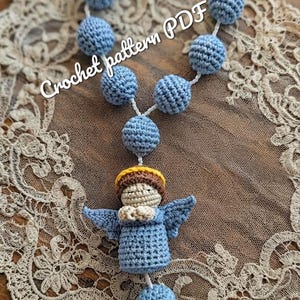 Puede incluir: Un rosario de ganchillo con cuentas esféricas de color azul claro y una figura central de ángel con cabello castaño, un halo amarillo y alas de color azul claro. El texto "Crochet pattern PDF" y "Yarnproductsua" es visible en la imagen.