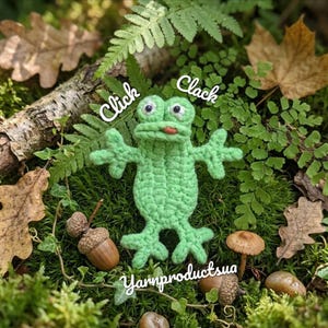 May include: A handmade green crochet frog with googly eyes and a red tongue, surrounded by moss, leaves, acorns, and a mushroom. The words "Click" and "Clack" are written above the frog, and "Yarnproductsua" is written below.