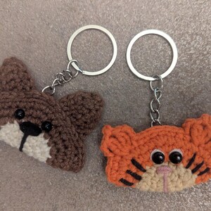 May include: Two crocheted animal keyrings, one brown and one orange, with black eyes and white noses. The keyrings are attached to silver key rings.
