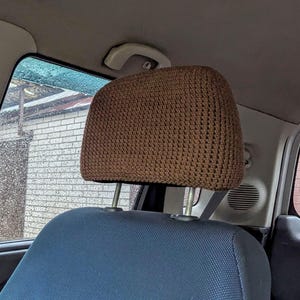May include: A brown crocheted headrest cover in a car. The cover has a textured surface and is a solid colour. The car seat below is blue.