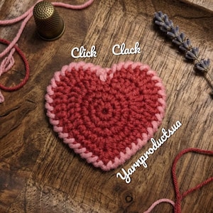 May include: A handmade, crocheted heart in shades of red and pink, with the words "Click Clack" and "Yarnproductsua" in the image. The heart is on a wooden tray, with a thimble, yarn, and lavender sprig.