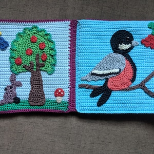 May include: Two crocheted squares, one depicting a green tree with red apples and a brown rabbit, the other depicting a blue bird with a red breast perched on a brown branch with red berries.