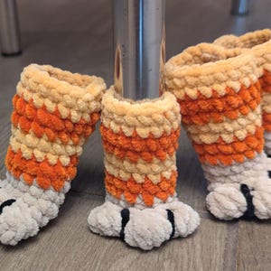 May include: Four crocheted orange and beige cat paw chair leg covers with black claws.