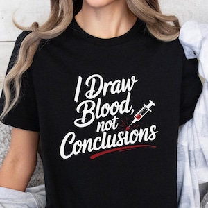 May include: Black t-shirt with the text "I Draw Blood, not Conclusions" in white script and a red syringe graphic. The shirt is a crew neck style.