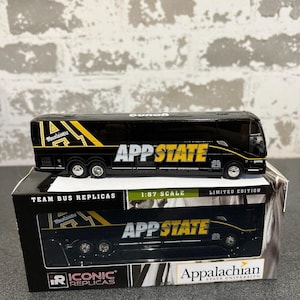 May include: A black and gold 1:87 scale die-cast replica of a team bus with "App State" and "Mountaineers" logos. The bus is on a display stand with the words "Team Bus Replicas", "Iconic Replicas", "Appalachian State University", and "Limited Edition".