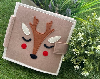 May include: A brown felt book with a white border. The front cover features a felt reindeer with closed eyes, brown antlers, and red cheeks.