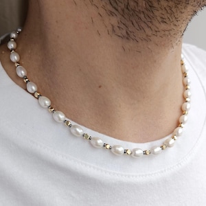 Könnte beinhalten: Eine weiße Perlenkette mit goldenen und schwarzen Akzenten. Die Kette besteht aus kleinen, runden Perlen und goldenen Perlen.