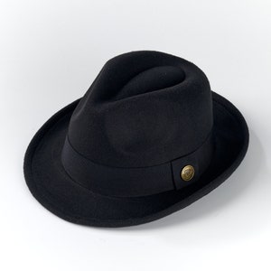 Könnte beinhalten: Ein schwarzer Fedora-Hut mit einem braunen Band und einem goldenen Knopf.