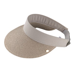 May include: A beige sun visor with a woven brim and a light grey band. The visor has a curved design and a small gold-coloured emblem on the side. The band is made of a soft material and is adjustable.