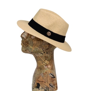 May include: A tan straw fedora hat with a black ribbon and a small brown logo on the front.