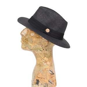 May include: A black fedora hat with a black ribbon and a gold button. The hat is made of a woven material and has a slightly curved brim.