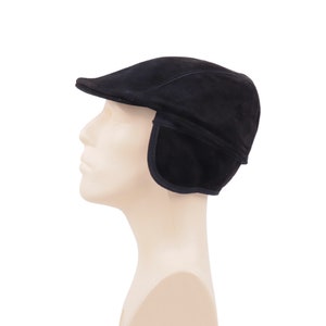 Peut inclure: Casquette plate en daim noir avec cache-oreilles. La casquette a une couronne arrondie et une petite visière rigide. Les cache-oreilles sont conçus pour protéger du froid. Présentée sur une tête de mannequin sur fond blanc.