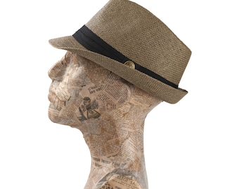 May include: A tan fedora hat with a black band and a gold button detail. The hat is displayed on a mannequin head covered in newspaper clippings. The hat has a structured brim and a woven texture.