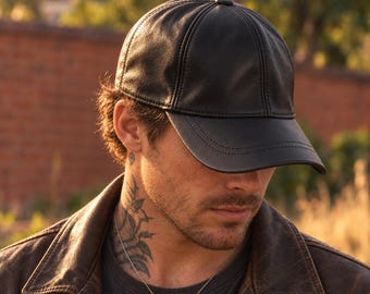 May include: A black leather baseball cap featuring a six-panel construction with visible stitching along the curved brim and a small button at the crown. The cap has a smooth, matte finish and a structured design that maintains its shape.