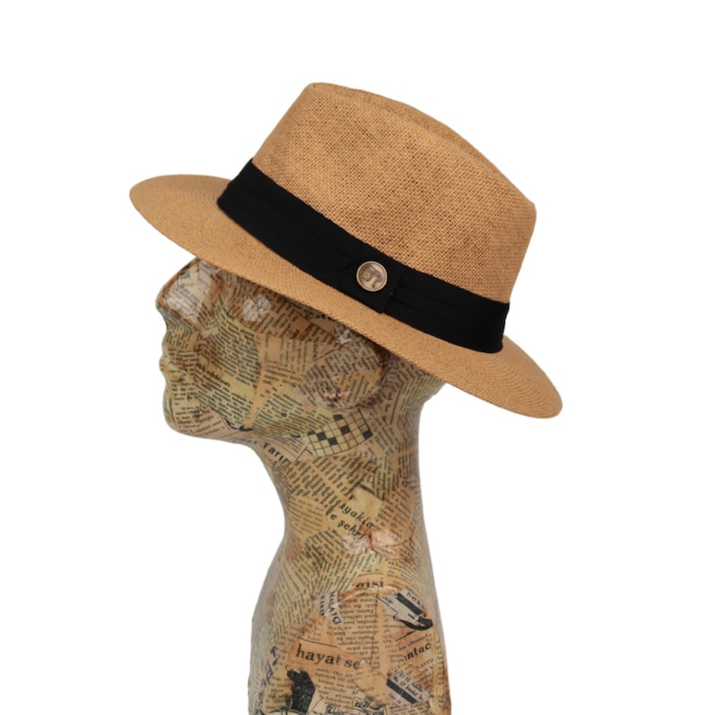 May include: A tan fedora hat with a black band and a gold button. The hat is made of straw and has a slightly curved brim.