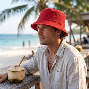 Op de afbeelding: Een effen rode bucket hat met een naar beneden hellende rand en stikseldetails rond de kroon. De hoed heeft een eenvoudig, ongestructureerd ontwerp met een platte bovenkant en een consistente levendige rode kleur in de stof.