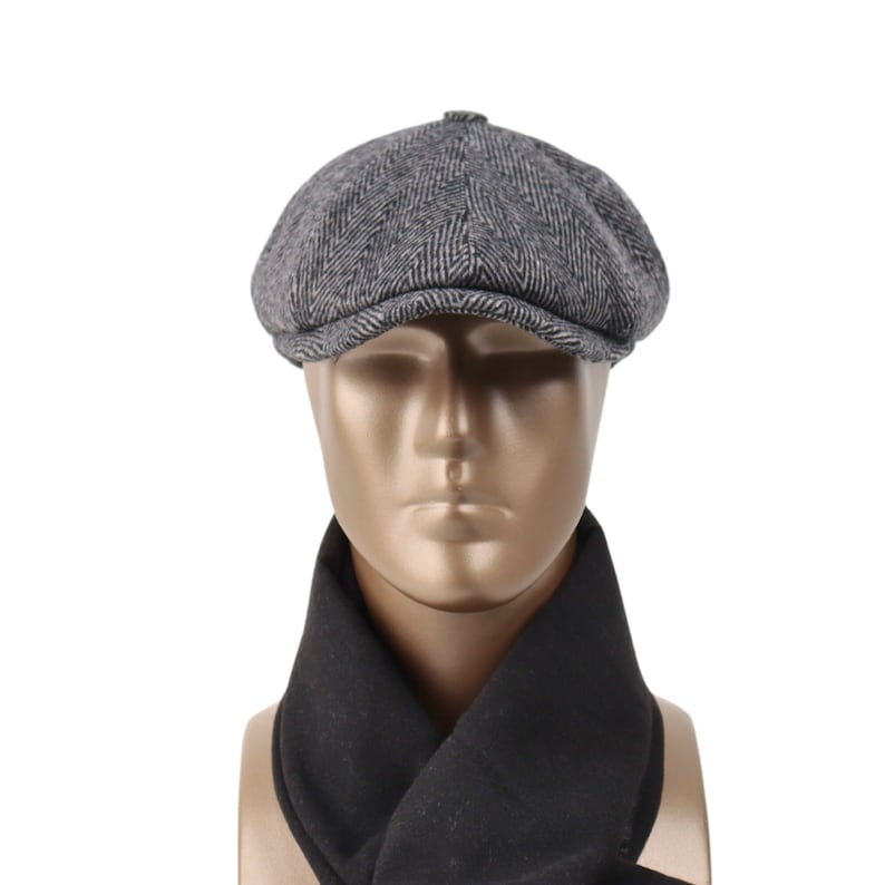 May include: A gray and black herringbone patterned newsboy cap with a black scarf.