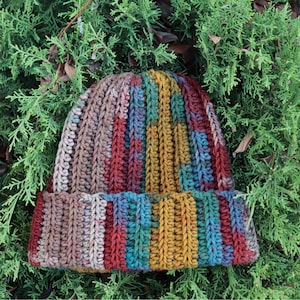 May include: A colorful crocheted beanie hat with stripes of brown, red, green, blue, and yellow yarn. The hat has a folded brim.