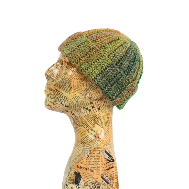 May include: A handmade, multi-colored crochet beanie hat. The hat features a ribbed design with shades of green, orange, and pink. The hat is displayed on a mannequin head with a newspaper print design.