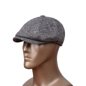 Puede incluir: Una gorra de golf de tweed gris con una corona redonda y una visera corta. La gorra está hecha de una tela suave y texturizada.