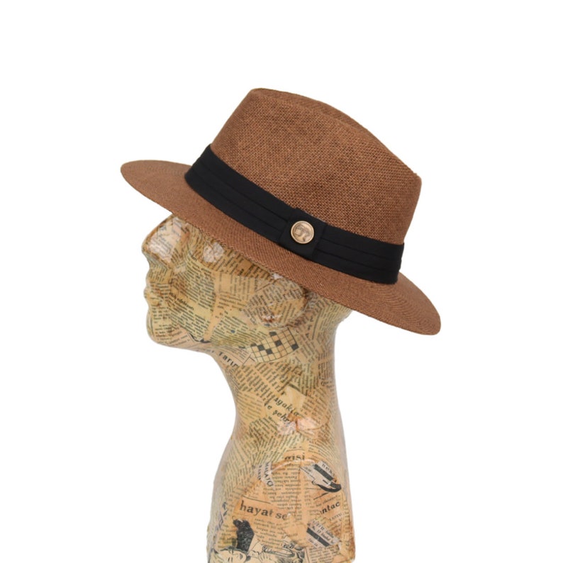 May include: A brown fedora hat with a black band and a gold button. The hat is made of a woven material and has a slightly curved brim.