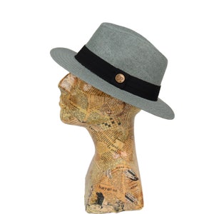 May include: A light gray fedora hat with a black band and a gold button. The hat is made of a woven material and has a slightly curved brim.