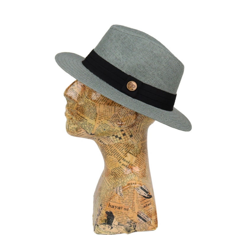 May include: A light gray fedora hat with a black band and a gold button. The hat is made of a woven material and has a slightly curved brim.