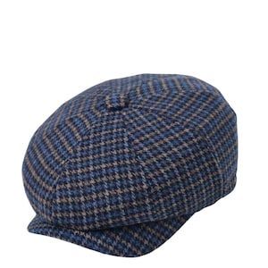 May include: A blue, tan, and black patterned newsboy cap. The cap features a classic houndstooth design and a small, rounded brim. The hat is made of a textured fabric.