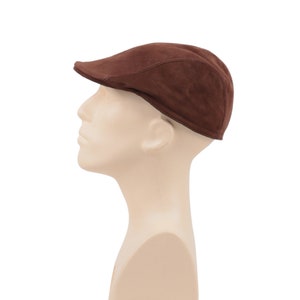 Könnte beinhalten: Eine braune, flache Mütze aus Wildleder auf einem Mannequin-Kopf.